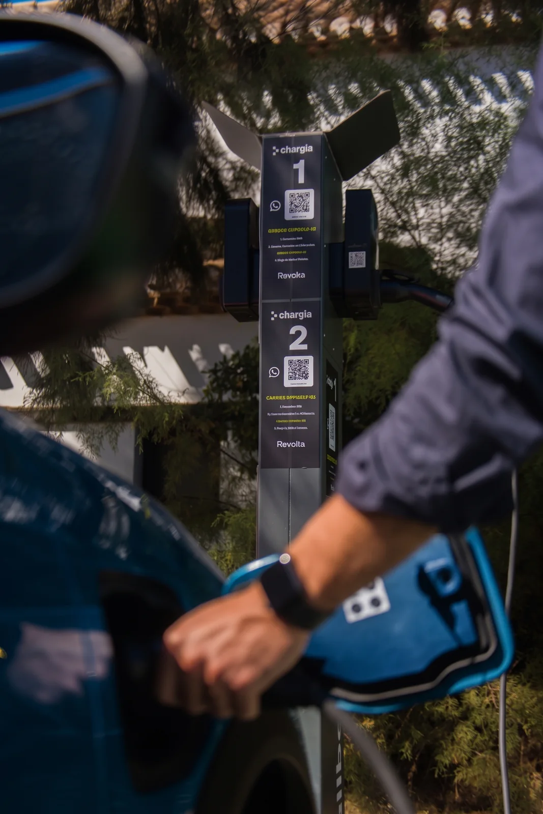 Mano conectando el cable al coche con el punto de recarga detrás